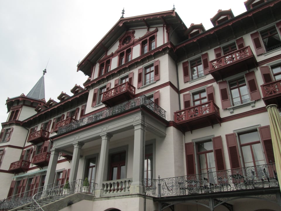 Ein älteres, gepflegtes, grosses Gebäude mit roten Fensterläden und roten Balkons.