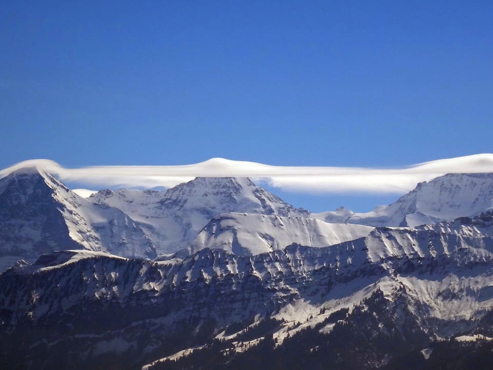 Der Himmel ist stahlblau. Nur über den Gipfeln der drei Berge liegt ein dichtes Wolkenband, welches von der Jungfrau über den Mönch bis zu Eiger reicht.