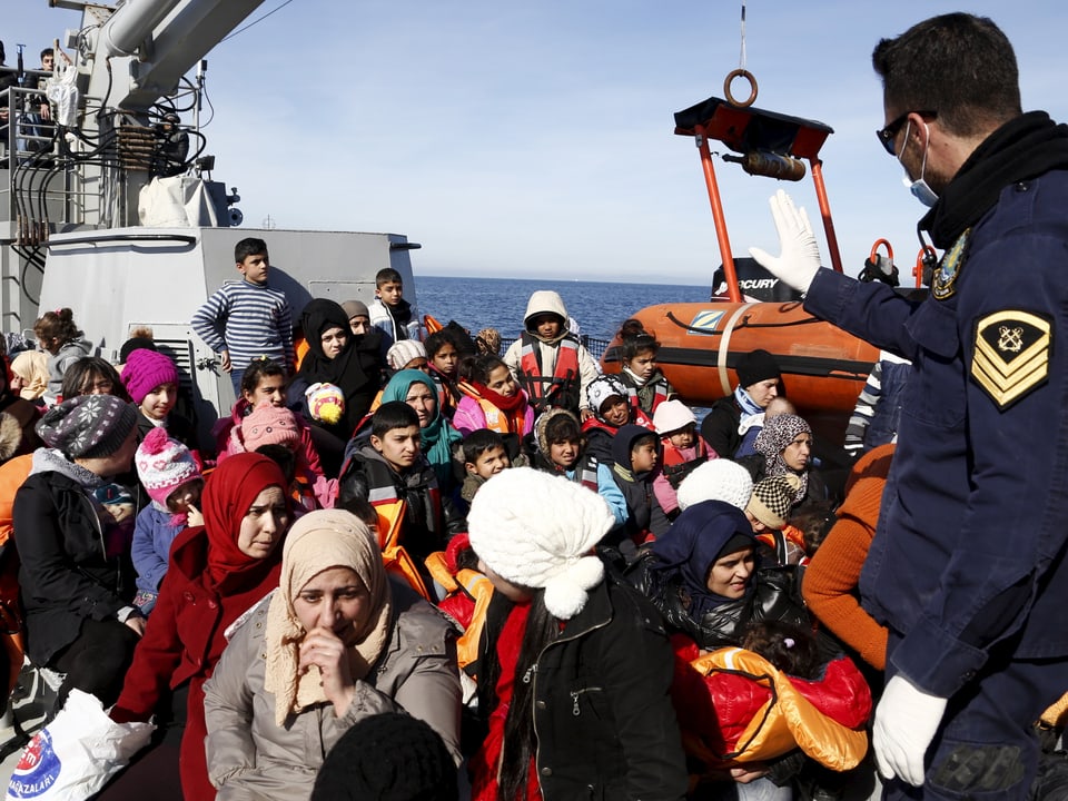 Dutzende Flüchtlinge auf einem grossen Schiff, ein uniformierter Mann steht im Vordergrund.