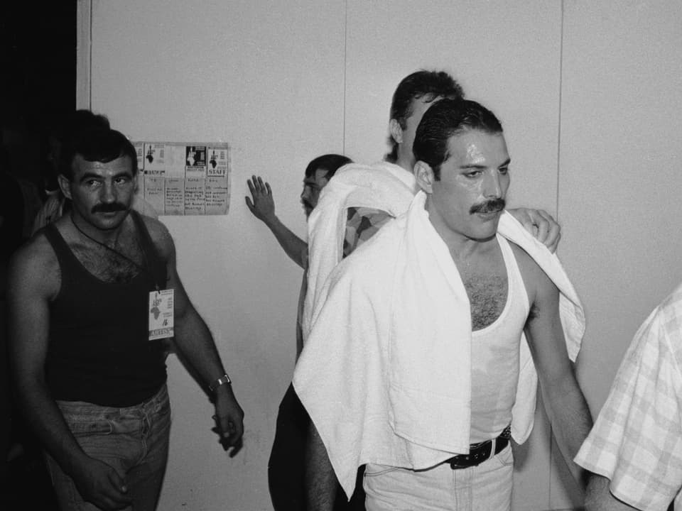 Freddie Mercury geht mit einem Schweisstuch auf seinen Schultern vermutlich in die Umkleidekabine.