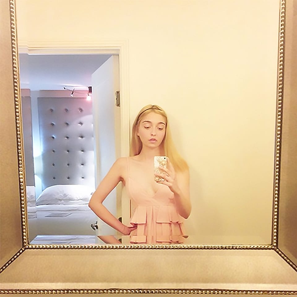 Eine junge Frau fotografiert sich mit dem Smartphine in einem grossen, goldgerahmten Spiegel. 
