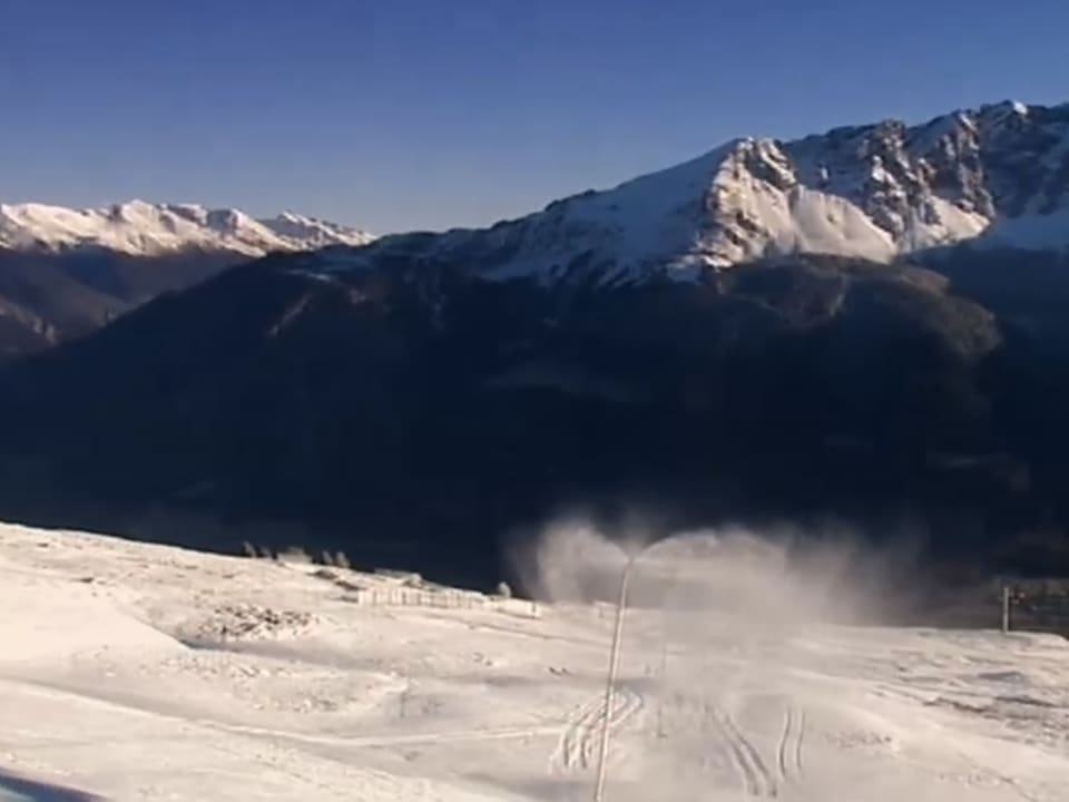 Ein Schneelanze in Betrieb, blauer Himmel, Blick auf die verschneiten Gipfel.