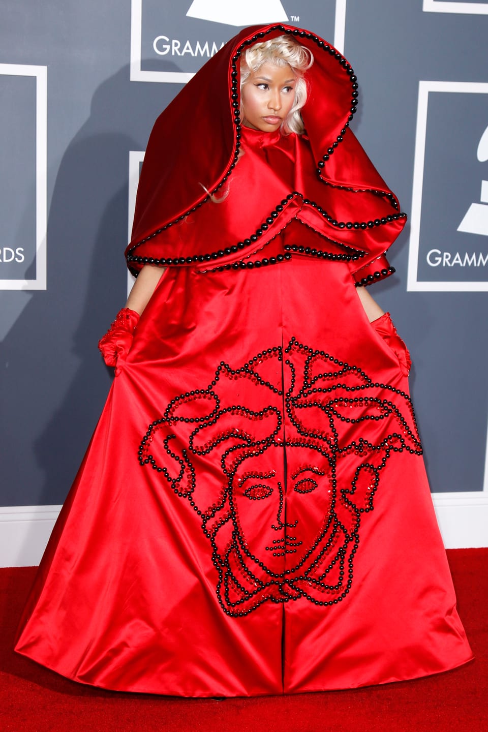 Nicki Minaj posiert in einem roten Umhang-Kleid auf dem roten Teppich.