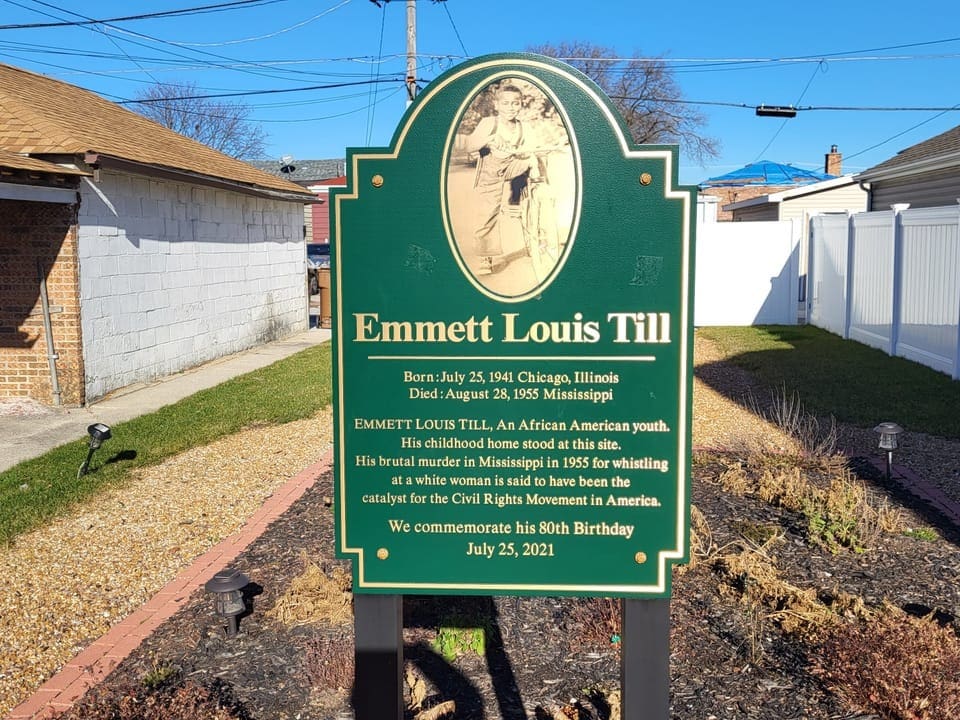 Foto einer dunkelgrünen Tafel, betitelt mit «Emmett Louis Till», dahinter Häuser und eine Wiese.