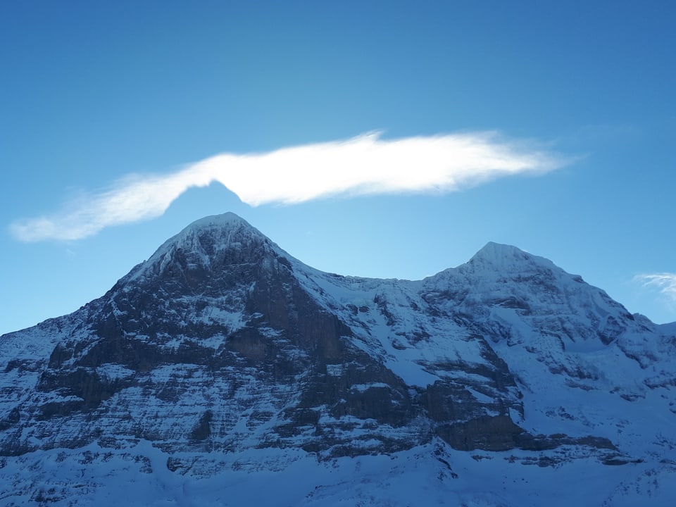 Schneeberge mit Felswand. Ein markanter Gipfel, eine Wolke darüber und darin der Schatten des Gipfels. 