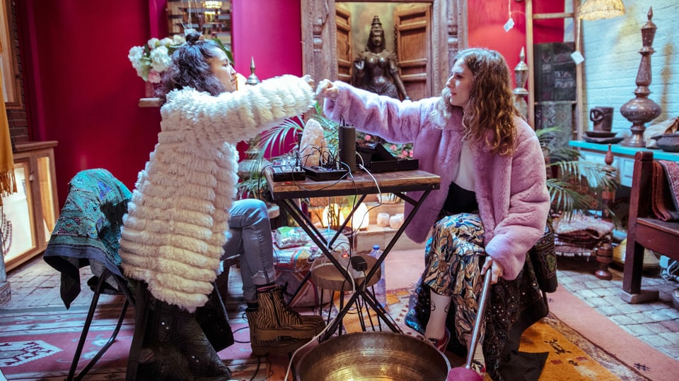 Zwei Frauen in flauschigen Mänteln sitzen an einem Tisch in einem üppig deokorierten Laden.