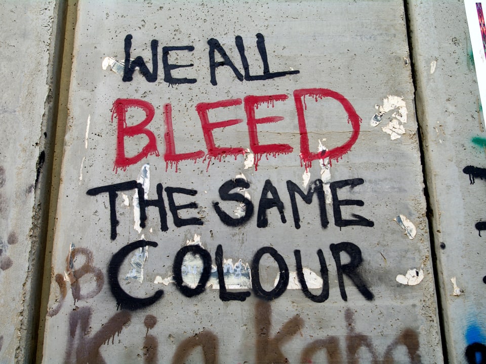 Schriftzug auf der Mauer mit rotem und schwarzem Spray: "We all bleed the same colour."