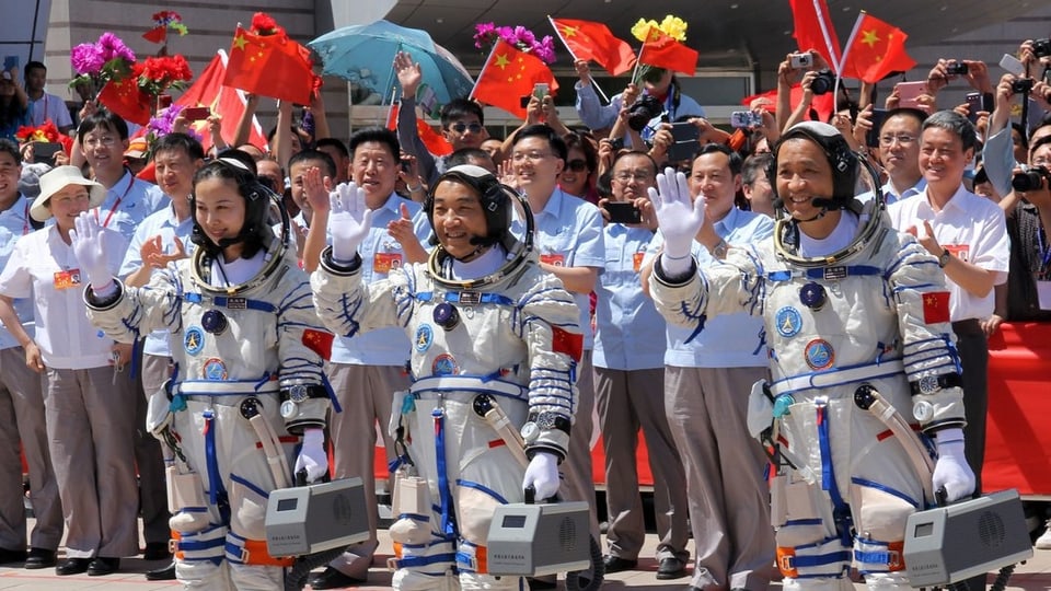 Drei Astronauten stehen winkend vor einer Menschenmenge.
