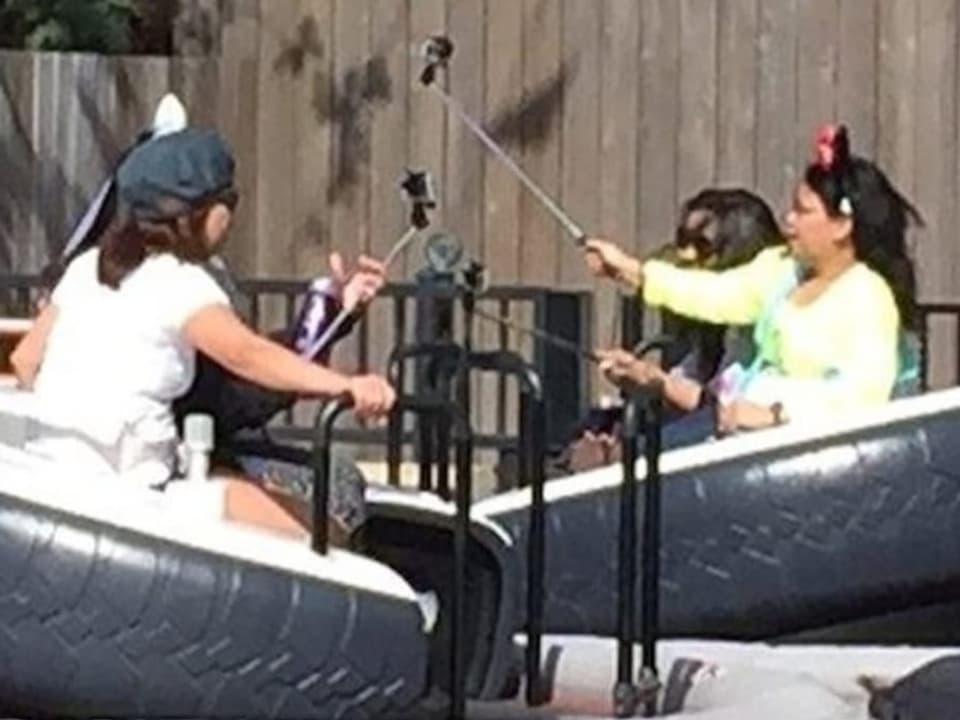 Drei Frauen halten Selfie Sticks auf einer Art Achterbahn