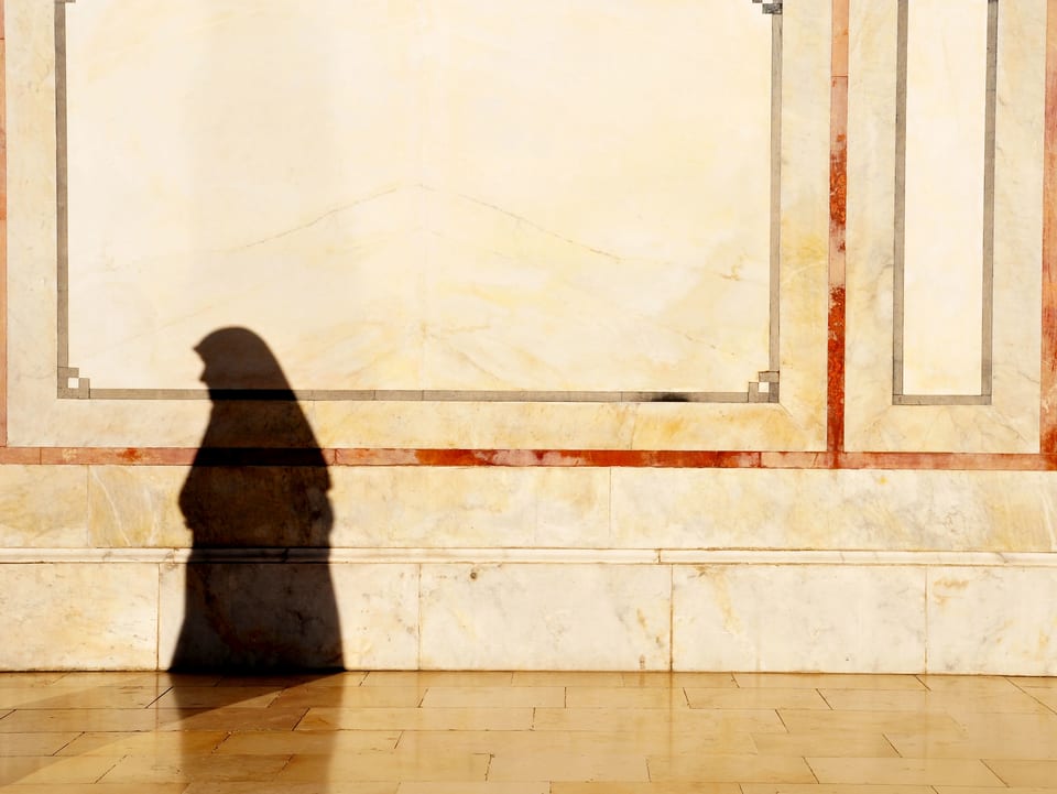 Eine verschleierte Frau wirft einen Schatten an eine dekorierte Hauswand.