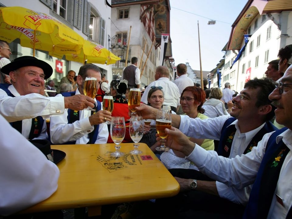 Jodler und Trachtenträger feiern in der Aarauer Altstadt an einem Festbank und trinken Bier.