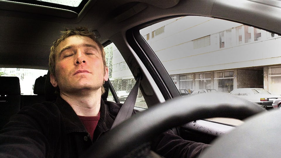 Mann sitzt mit geschlossenen Augen am Steuer eines Autos.