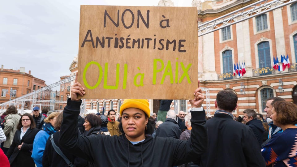 Eine Demonstrantin hält ein Schild hoch, worauf übersetzt auf Deutsch steht: Nein zum Antisemitismus, Ja zum Frieden.