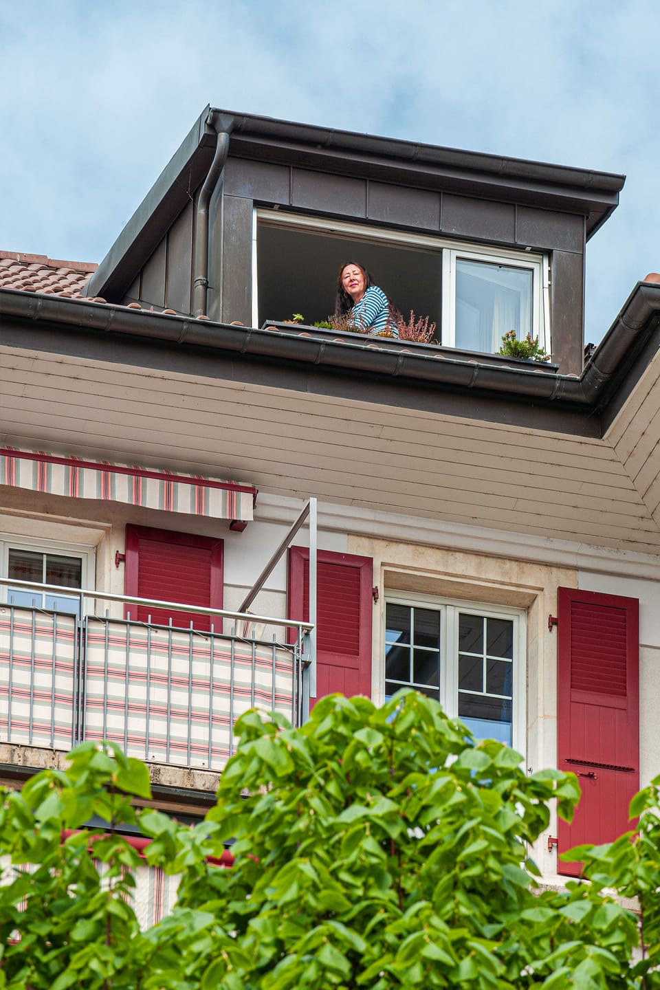 Eine Frau sitzt an ihrem Dachfenster und blickt zum Fotograf hinunter.