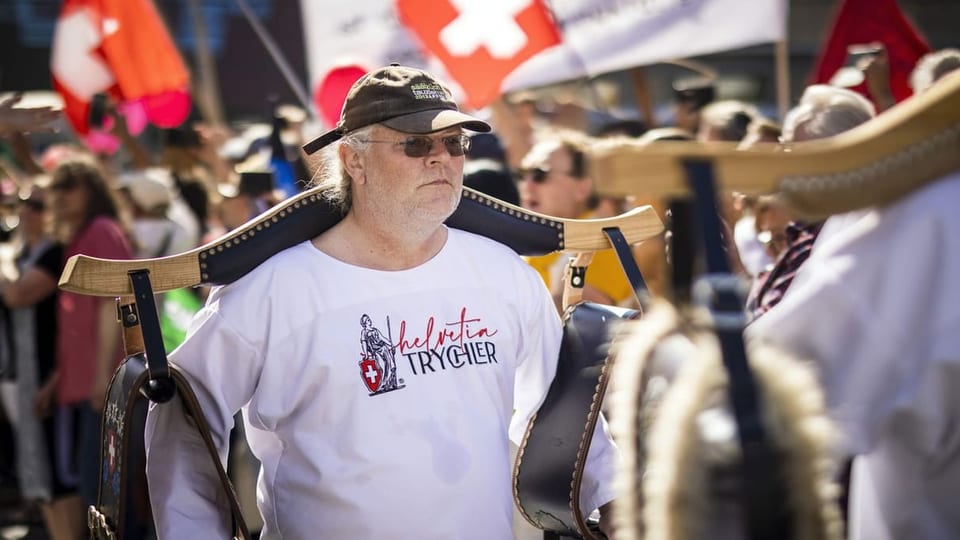 Ein Mann mit grosser Glocke auf den Schultern. Auf seinem weissen Shirt steht: Helvetia-Trychler.