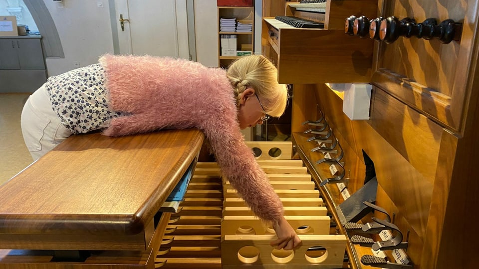 Mädchen befestigt Holzklötze an Pedalen einer Kirchenorgel