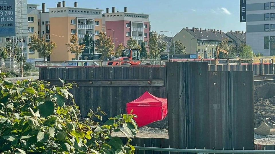 Blick auf eine Baustelle mit einem roten Zelt, im Hintergrund Wohnblocks