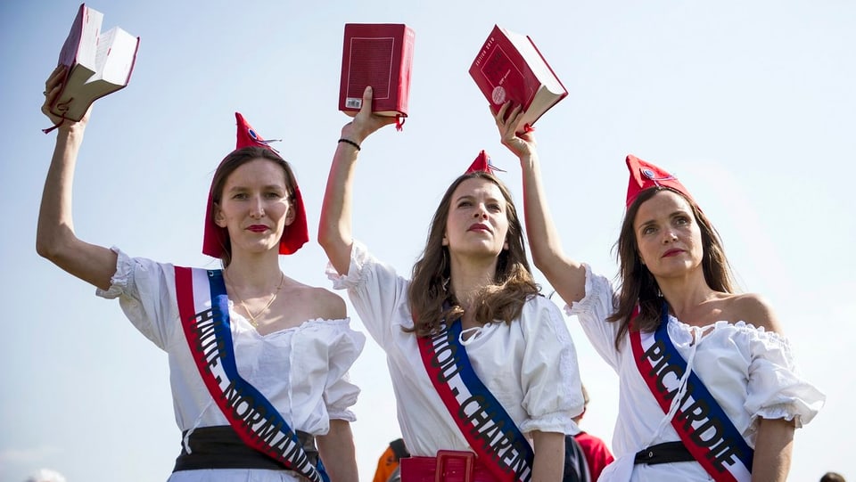 Drei Frauen als Marianne verkleidet halten jeweils das französische Gesetz in der Hand