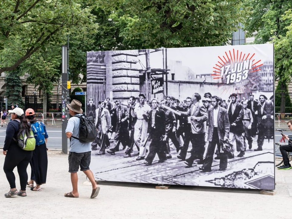 Menschen laufen an einem übergrossen Abbild des Aufstandes 1953 vorbei