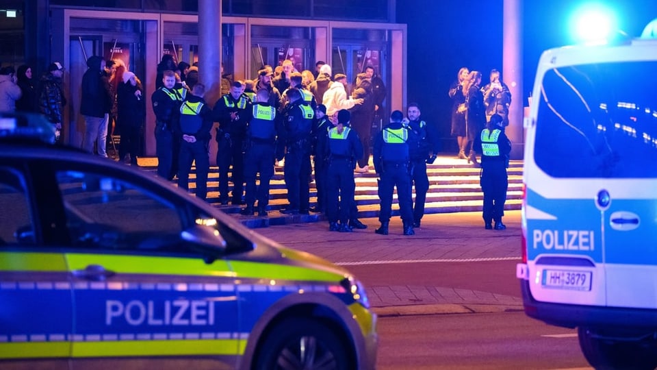 Menschen vor einem Kino in Hamburg und viele uniformierte Polizisten. Im Vordergrund Polizeiwagen.