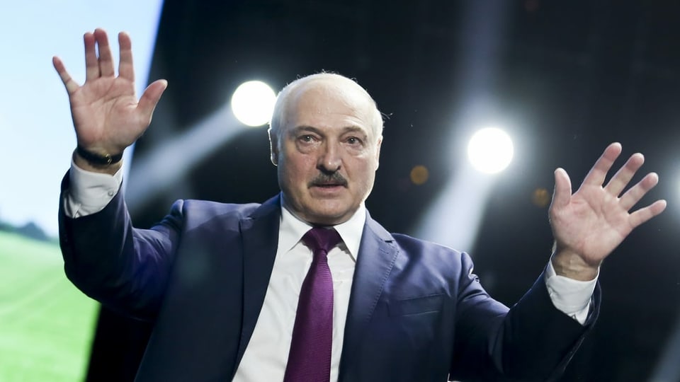 Lukaschenko hat beide Hände erhoben und blickt in die Ferne.