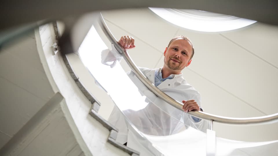 Porträt Collin Ewald, der von einer Wendeltreppe runterblickt.