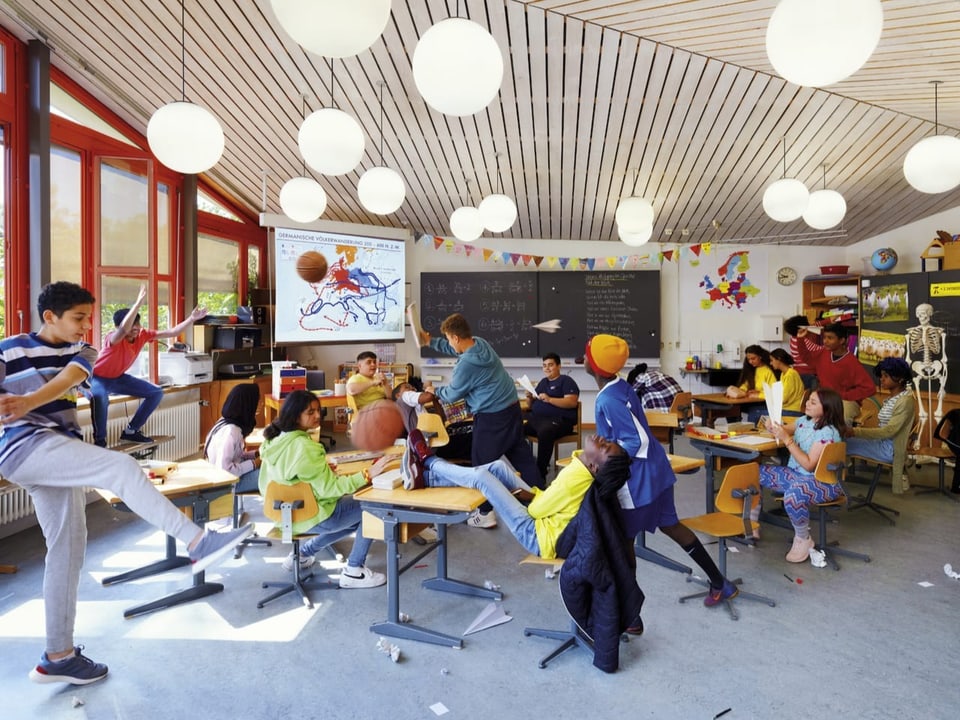 Blick in ein Klassenzimmer. Schülerinnen und Schüler tollen herum.