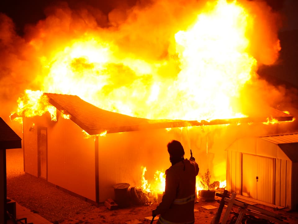 Ein Feuerwehrmann versucht ein in Flammen stehendes Haus zu löschen. 
