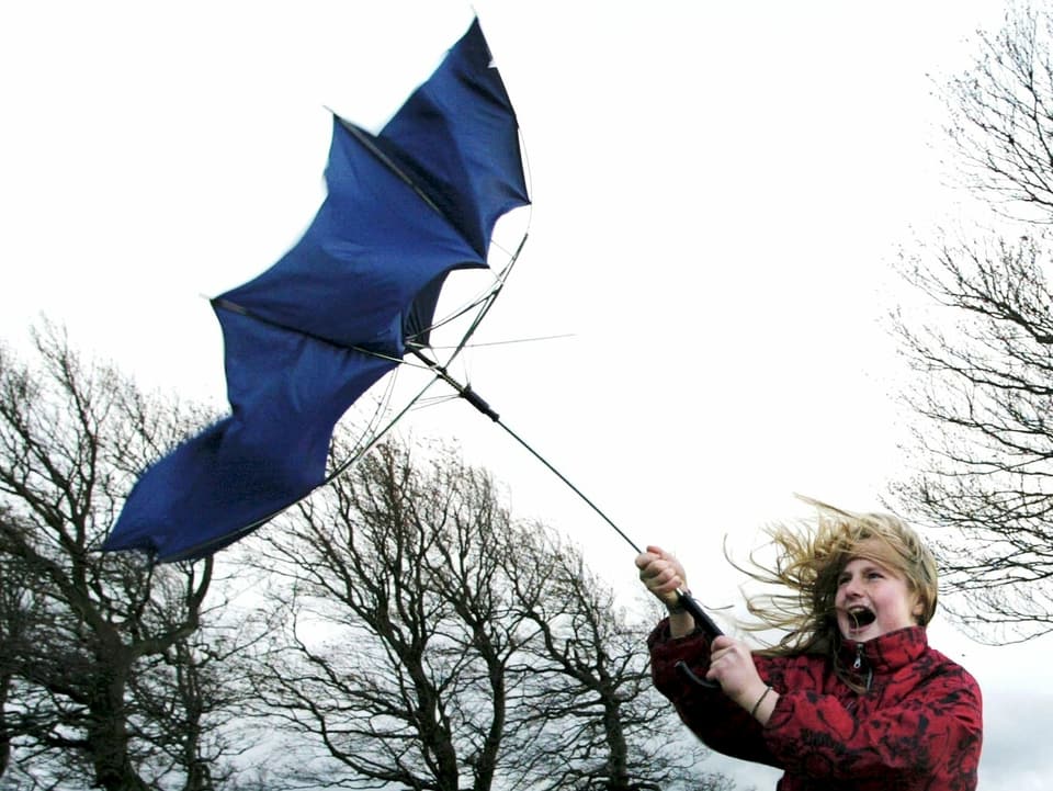Ein blauer Schirm in der Hand eines Mädchen klappt im Sturm um.