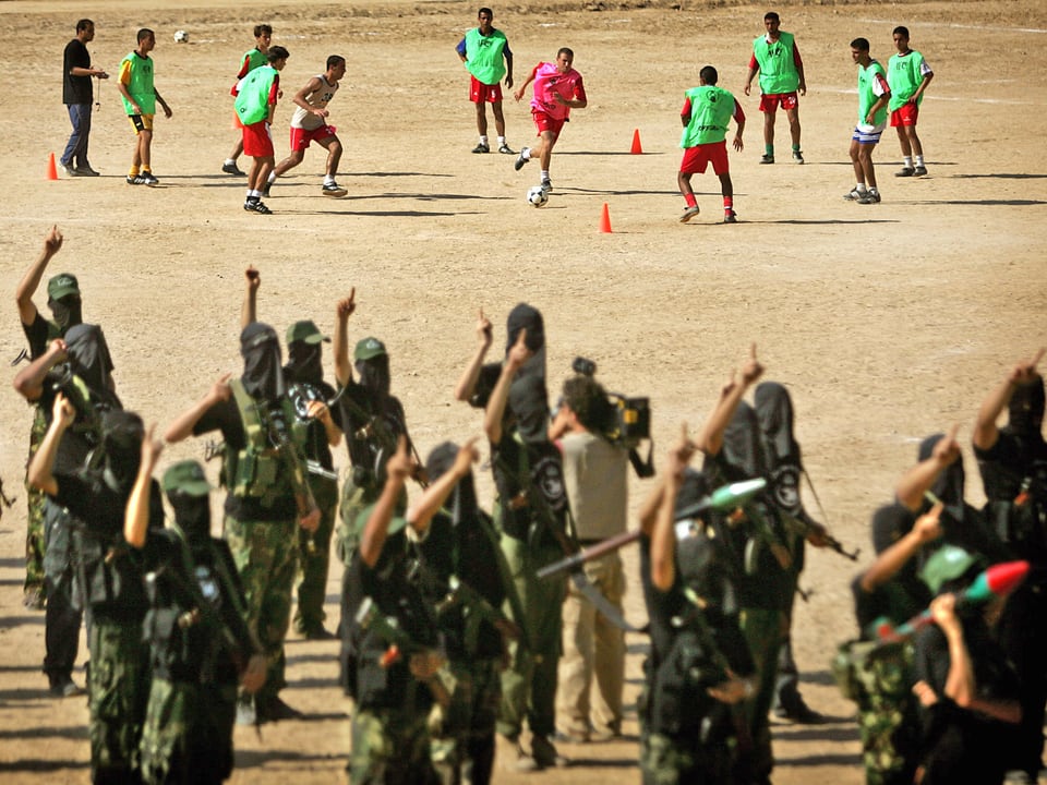Im Hintergrund trainieren palästinensische Spieler, vorne exerziert eine Miliz. 