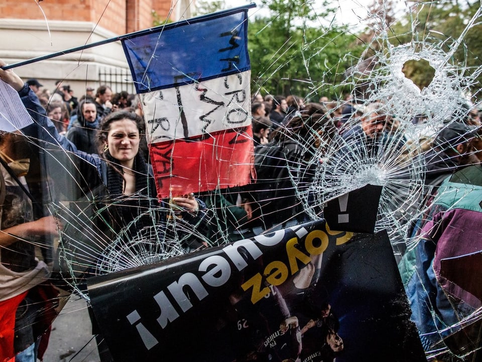 Eine Demonstrantin hinter einer zersplitterten Fensterscheibe