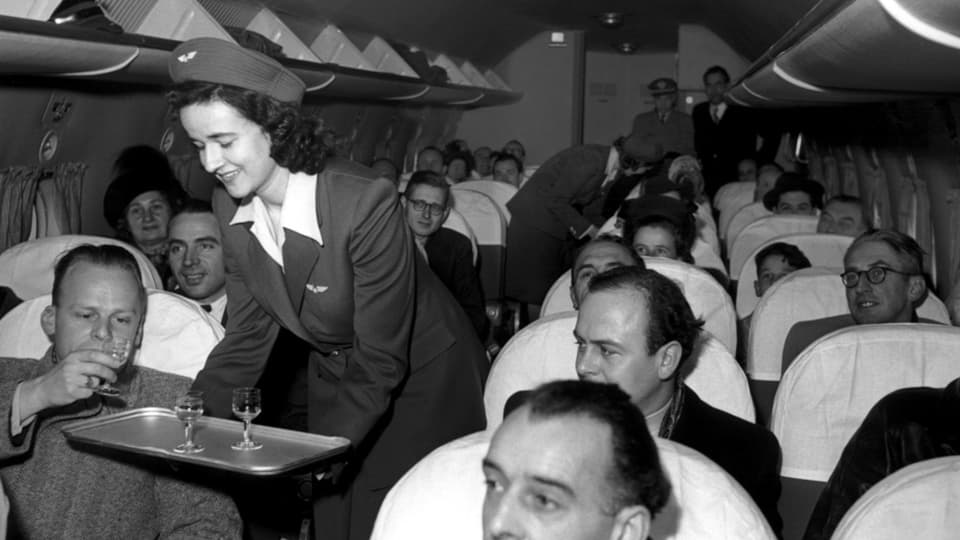 Stewardess in Uniform bedient ein Flugzeug voller Männer