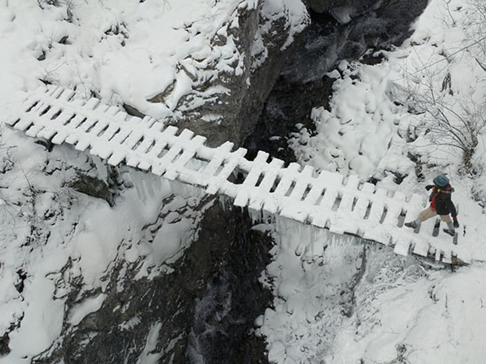 Schellenursli geht über eine verschneite Holzbrücke über der Schlucht.