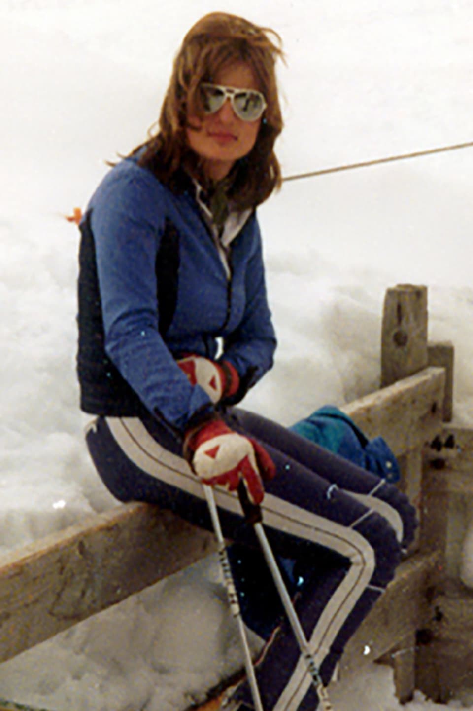Heidi van Straaten sitzt während den 80er auf einer Absperrung in einem Skigebiet.