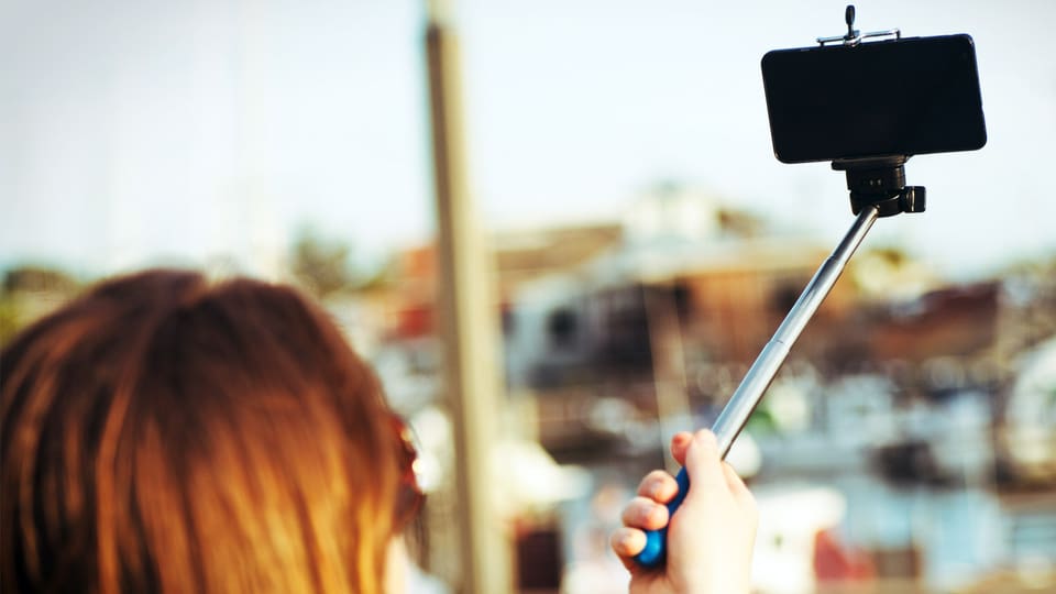 Frau macht ein Selfie mit ihrem Smartphone an einem Selfie-Stick.