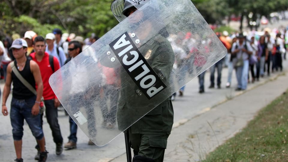 Ein kolumbianischer Polizist im Vordergrund, dahinter sind Protestierende.