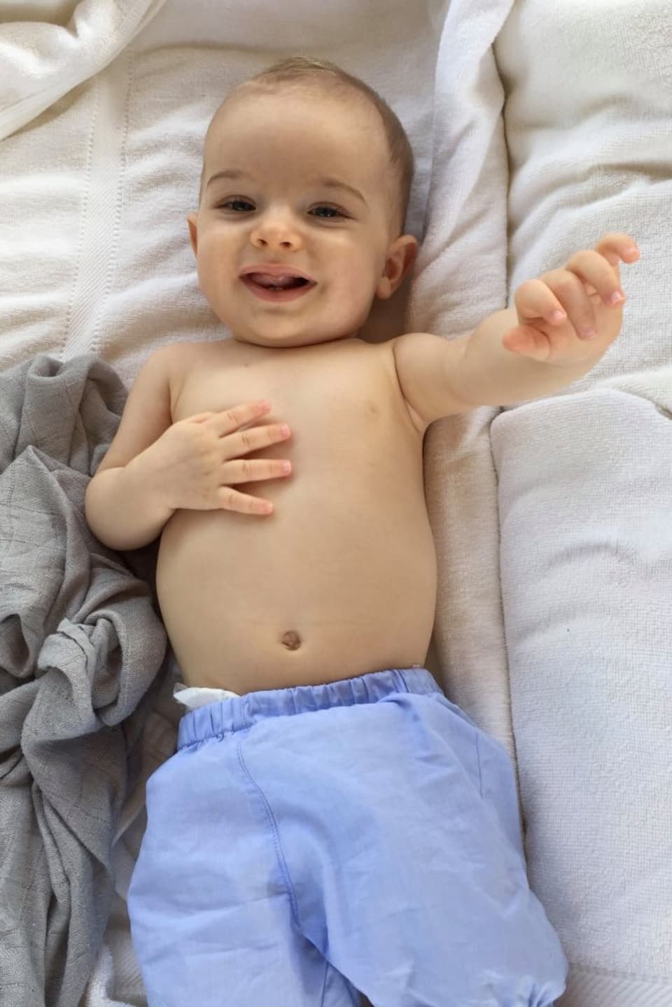 Lachendes Baby in blauen Shorts auf einem Tuch liegend.