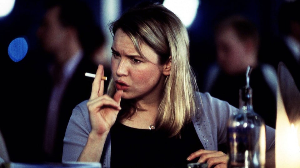 Filmszene: Eine junge Frau sitzt an einem Tisch und raucht. Vor ihr steht eine Flasche Vodka.