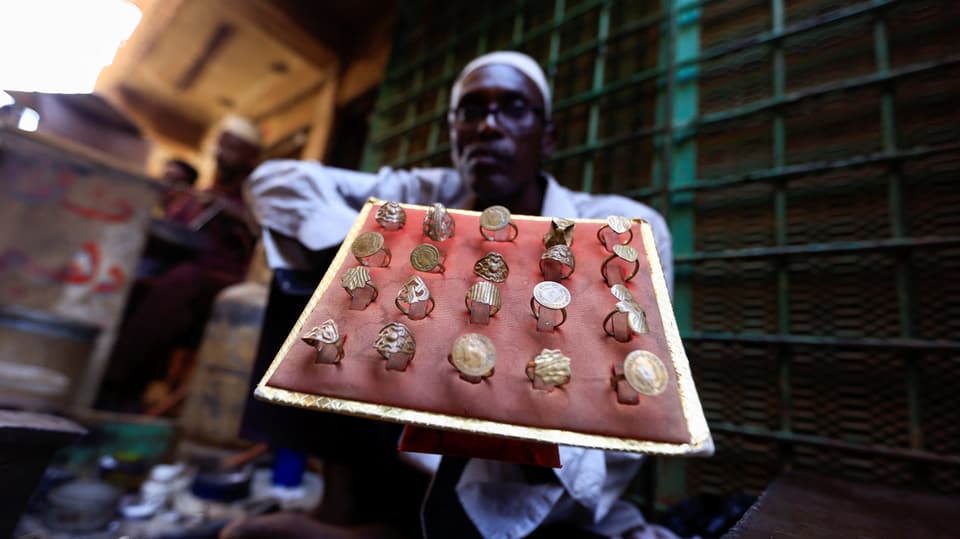 Ein Mann auf einem Markt in Sudan präsentiert eine Auswahl an Gold-Fingerringen.