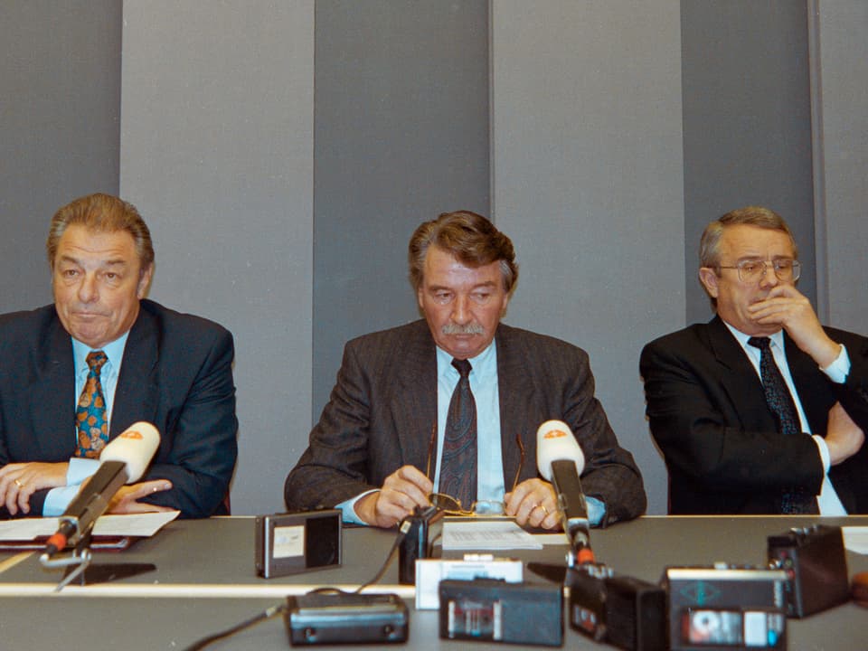Arnold Koller und zwei Politiker sitzen an einem Tisch vor Mikrophonen