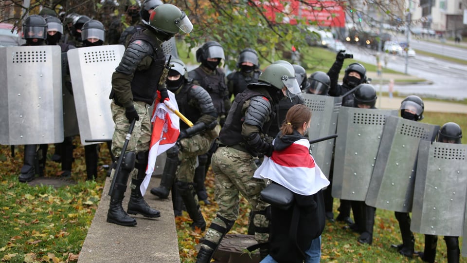 Polizisten in Vollmontur führen eine junge Frau mit rot-weiss-roter Flagge ab.