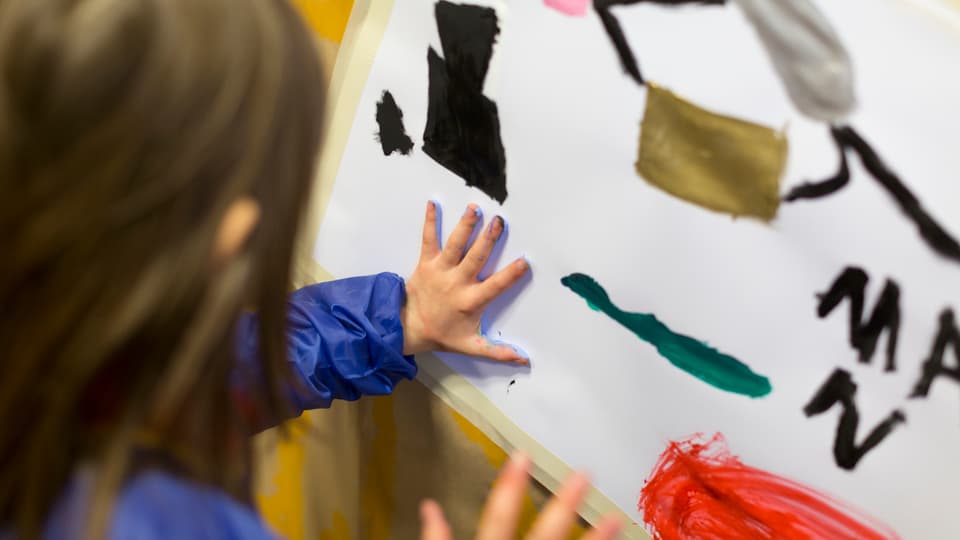 Kind drückt Hand mit Farbe auf ein Blatt Papier