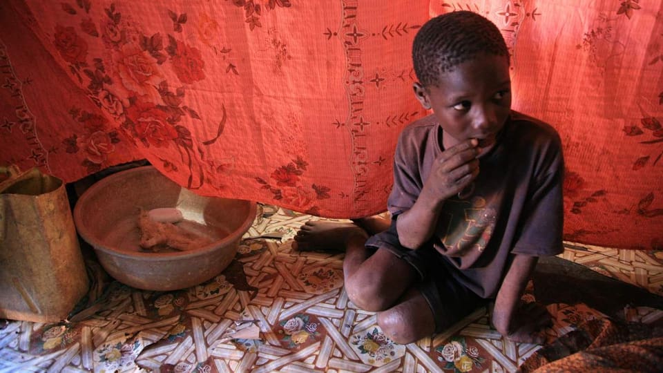 Ein dunkelhäutiges Kind aus Uganda sitzt in einem Zelt.