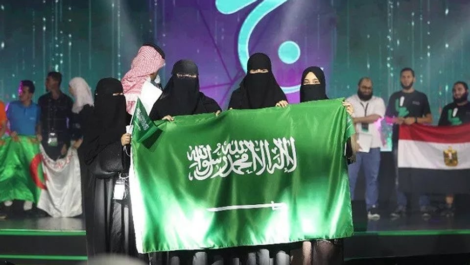 Vier verschleierte Frauen halten bei einer Preisverleihung. die Landesfahne Saudi-Arabiens in die Kamera.
