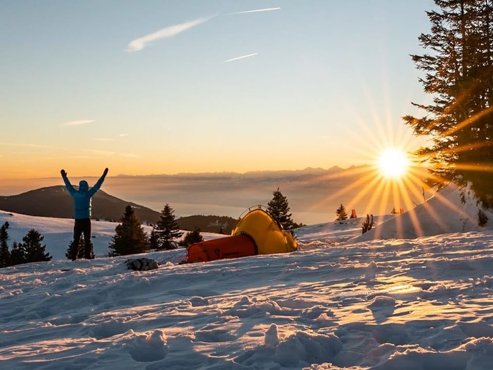 Sonnenaufgang im Schnee mit Zelt und Mann in blauer Jacke