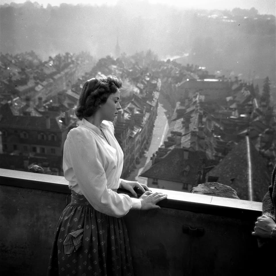 Eine Frau (Jeanette) steht an einer Mauer überhalb der Stadt im Hintergrund. 