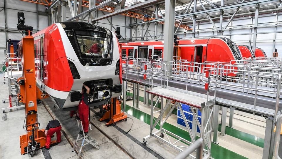 Bombardier Transportation in Deutschland, Blick ins Produktionslager, wo Arbeiter an zwei Zügen arbeiten.