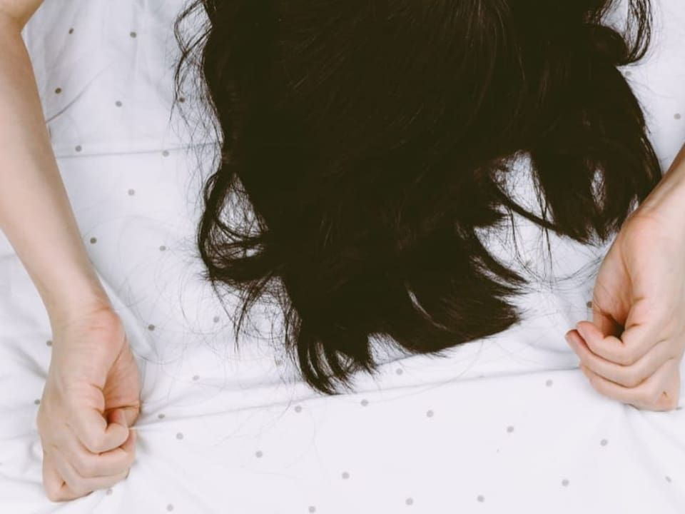 Eine Frau liegt auf dem Bett mit den Händen über dem Kopf.