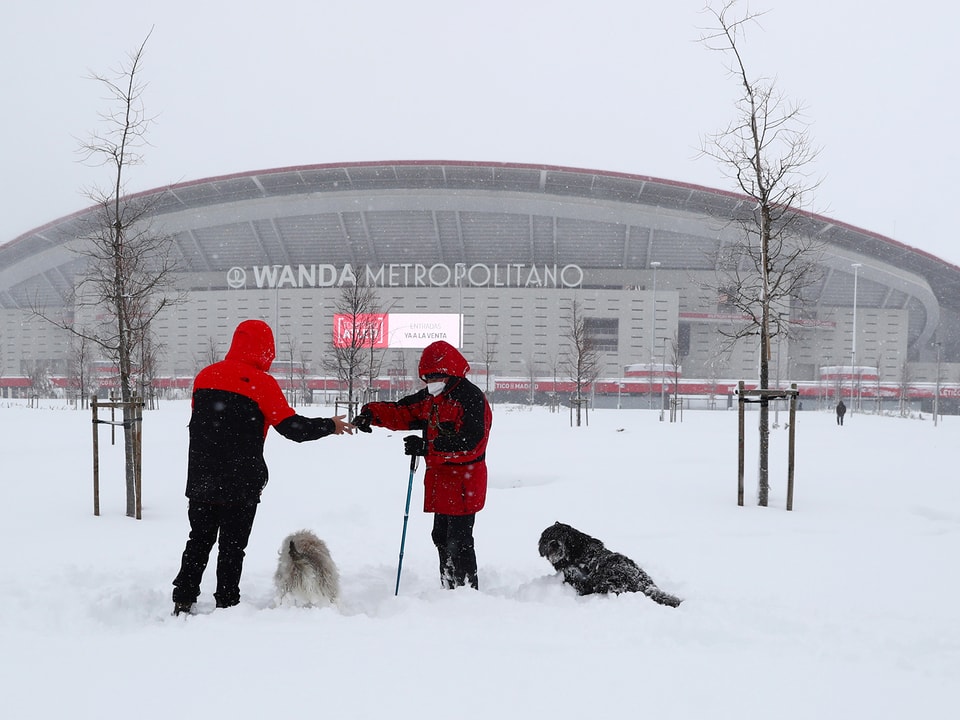 Spaziergänger mit Hunden im Schnee vor dem Stadion von Atletico Madrid. 