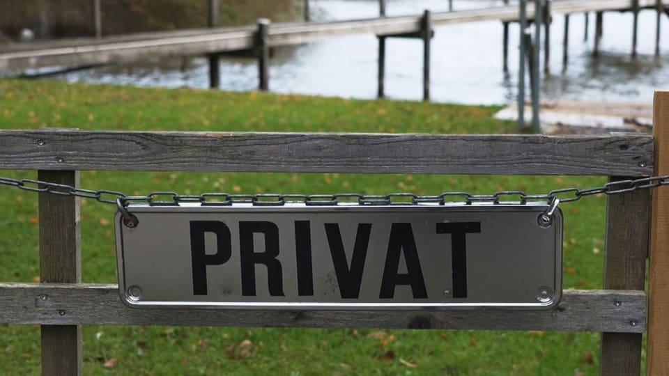 Schild mit der Aufschrift «Privat» an einem Zaun, im Hintergrund ein Bootssteg.